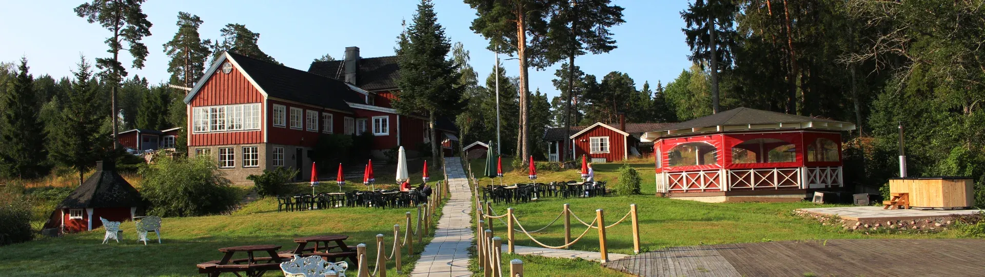 Odalgårdens byggnader och öppna gräsmattor en sommardag, med skogen runt omkring.