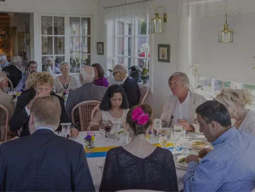 Festsällskap som sitter och äter tillsammans vid ett dukat långbord med blommor på.
