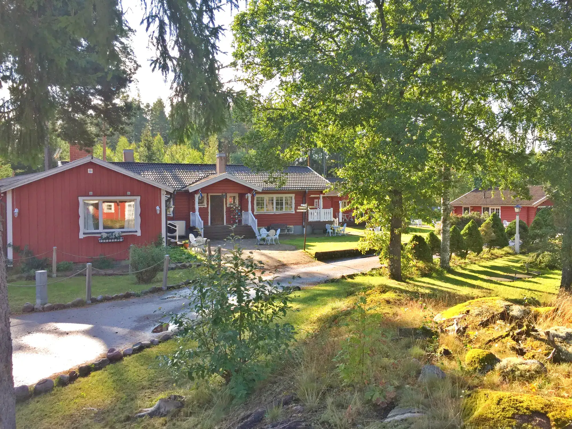 Röda stugor i stugbyn bland gröna träd och gräsmattor en solig sommardag.