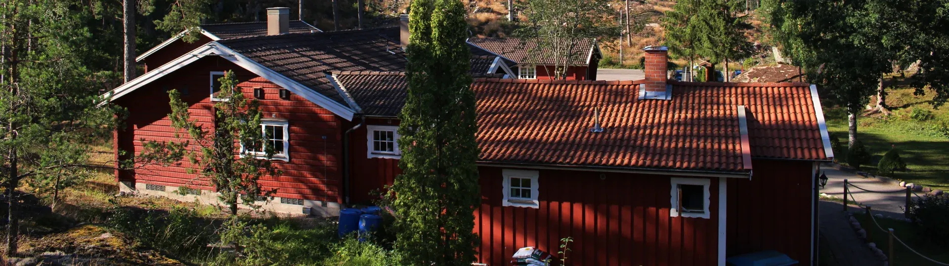Röda stugor med vita fönsterfoder bland träden på Odalgårdens område.